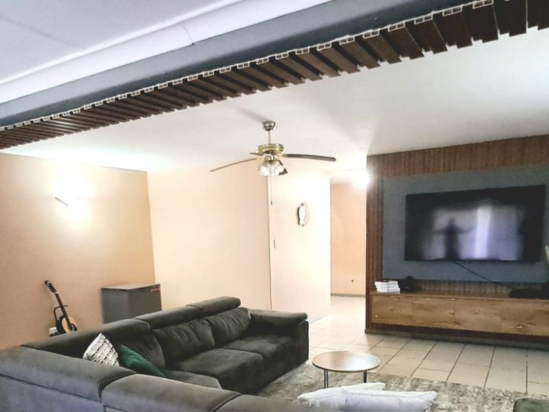 Spacious living room featuring tiled flooring, a ceiling fan, and a built-in media console with decorative timber ceiling detailing.