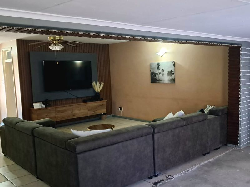 A living room featuring tiled flooring, a ceiling fan, and a decorative wall paneling feature with a built-in television mount.
