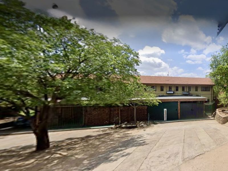 Street view of the apartment complex featuring a brick boundary wall, tiled roof, and garage access.