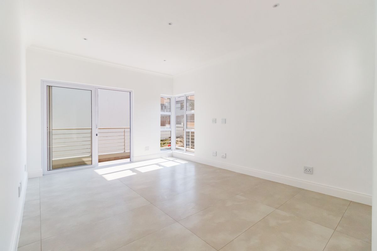 A bright, empty living room featuring large format floor tiles, modern corner windows, and a sliding door leading to an outdoor balcony area.