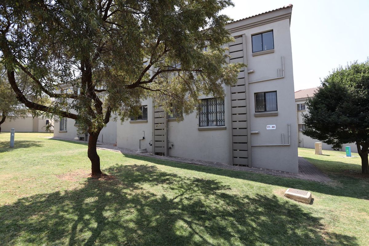 Rear view of the apartment building showing the exterior facade, security bars on windows, and surrounding landscaped garden area.