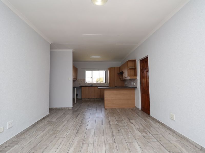 An open-plan living and kitchen area featuring light wood-look laminate flooring, neutral walls, and a functional kitchen with built-in cabinetry and a peninsula.