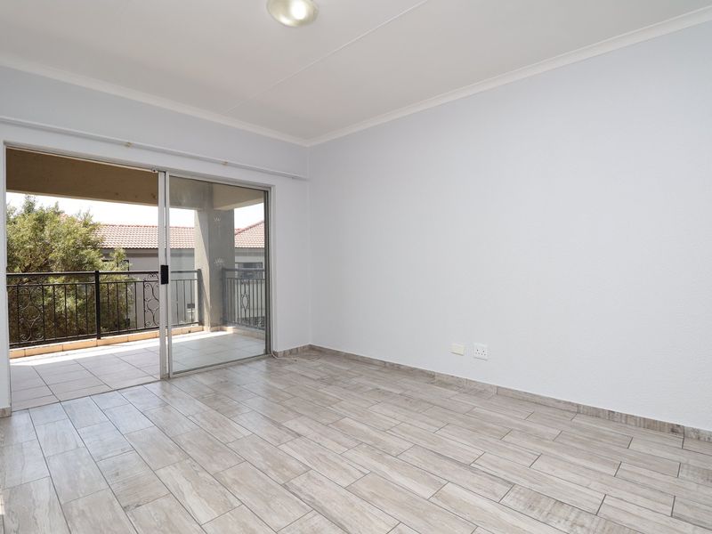 Bright and spacious living area featuring modern wood-look tiled flooring and large sliding glass doors leading to a private balcony.