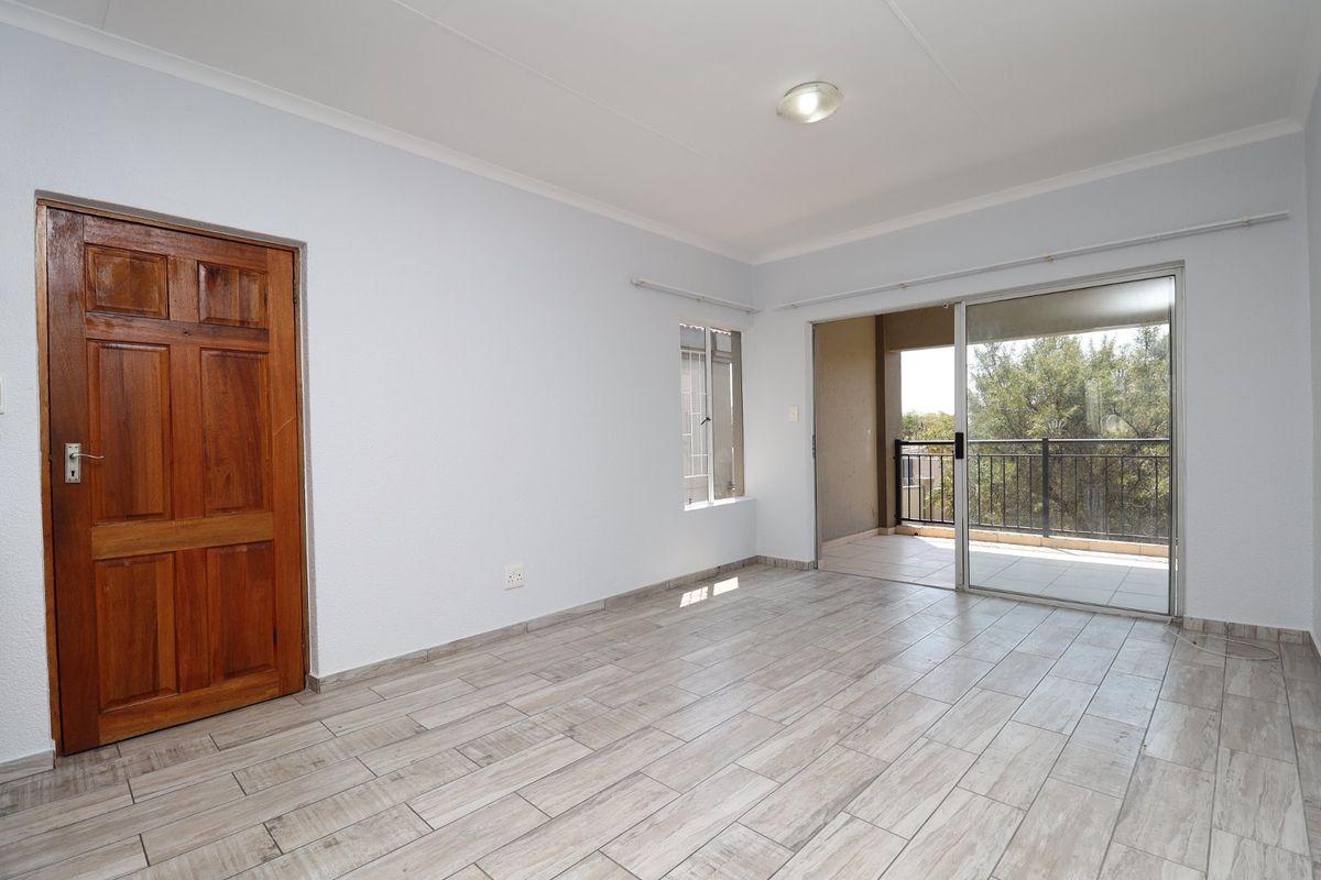 An empty living room featuring light-toned tiled flooring, a wooden door, and large sliding glass doors providing access to an outdoor balcony.