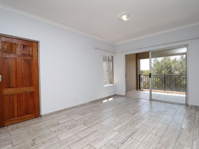 An empty living room featuring light-toned tiled flooring, a wooden door, and large sliding glass doors providing access to an outdoor balcony.