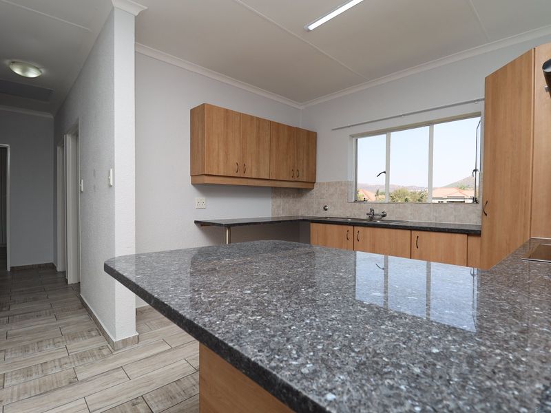 A clean, functional kitchen featuring granite countertops, laminate cabinetry, and a tiled backsplash with a view through the window.