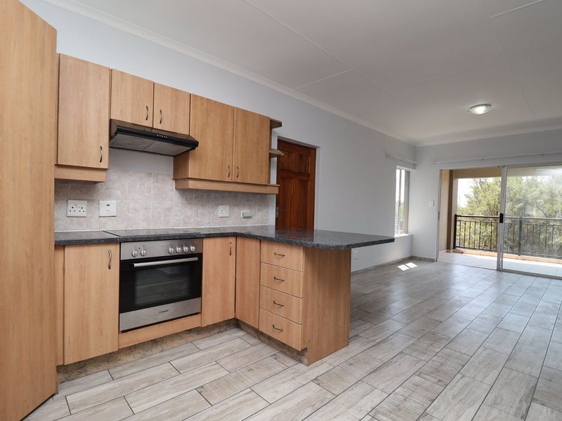 Open-plan kitchen and living area featuring light wood cabinetry, built-in oven, tiled flooring, and direct access to a private balcony.