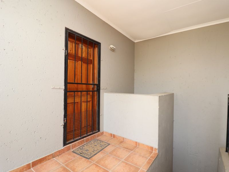 A private apartment entrance featuring a wooden door with a security gate, tiled landing, and metal balustrade.