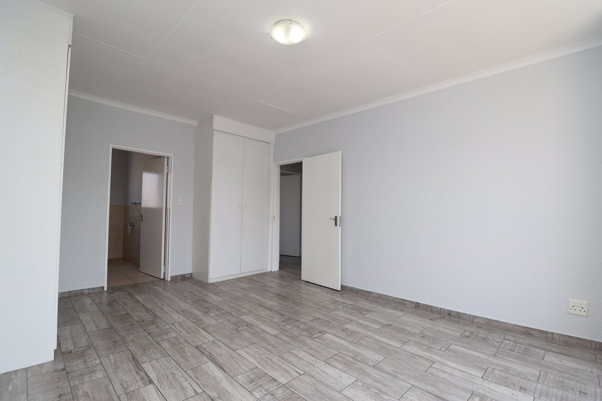A bright, empty bedroom featuring modern wood-look tiled flooring, built-in cupboards, and neutral wall finishes, providing a clean canvas for personalization.