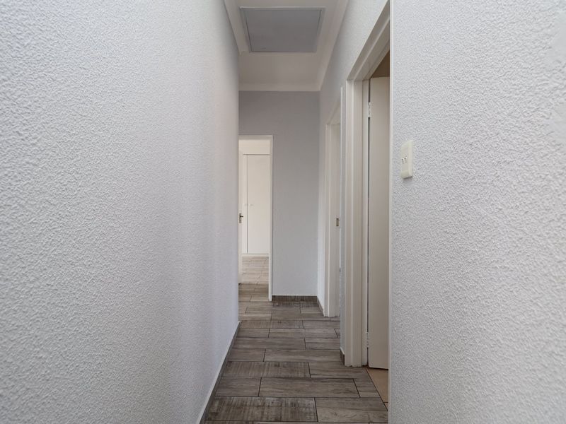 A clean, well-maintained hallway featuring textured walls and modern wood-look floor tiles, providing access to multiple rooms.