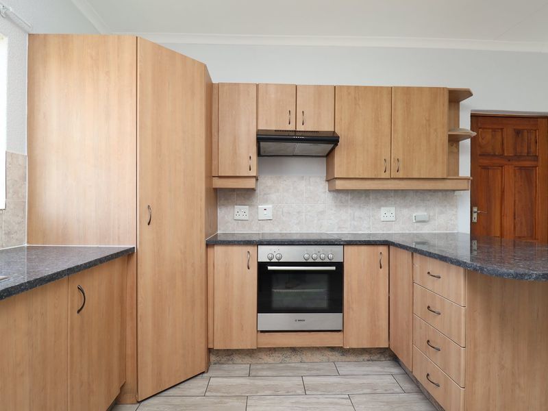 A clean and functional kitchen featuring light wood laminate cabinetry, granite countertops, a built-in oven, and an extractor fan with neutral tiled flooring.