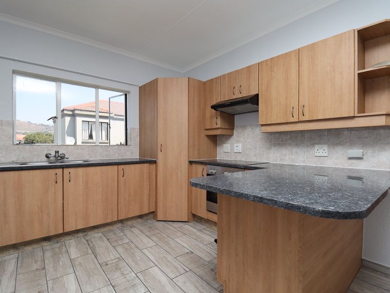 A functional kitchen featuring light wood-look cabinetry, granite countertops, a built-in oven with extractor fan, and neutral tiled flooring.