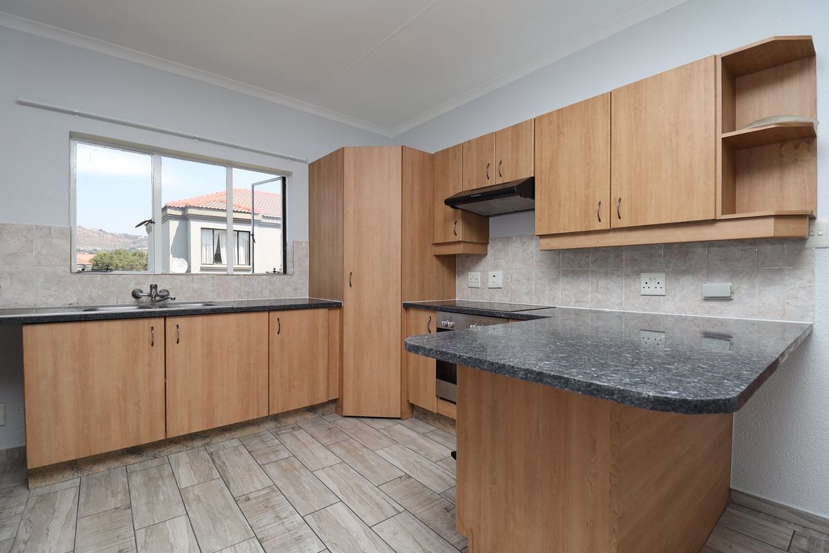 A functional kitchen featuring light wood-look cabinetry, granite countertops, a built-in oven with extractor fan, and neutral tiled flooring.