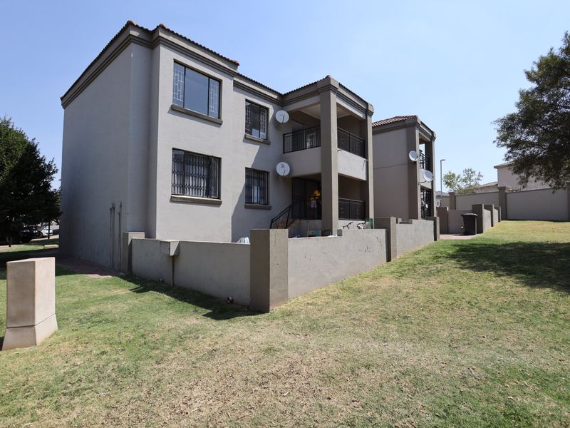 Rear view of a multi-story apartment building featuring balconies, security bars on windows, and a shared garden area.