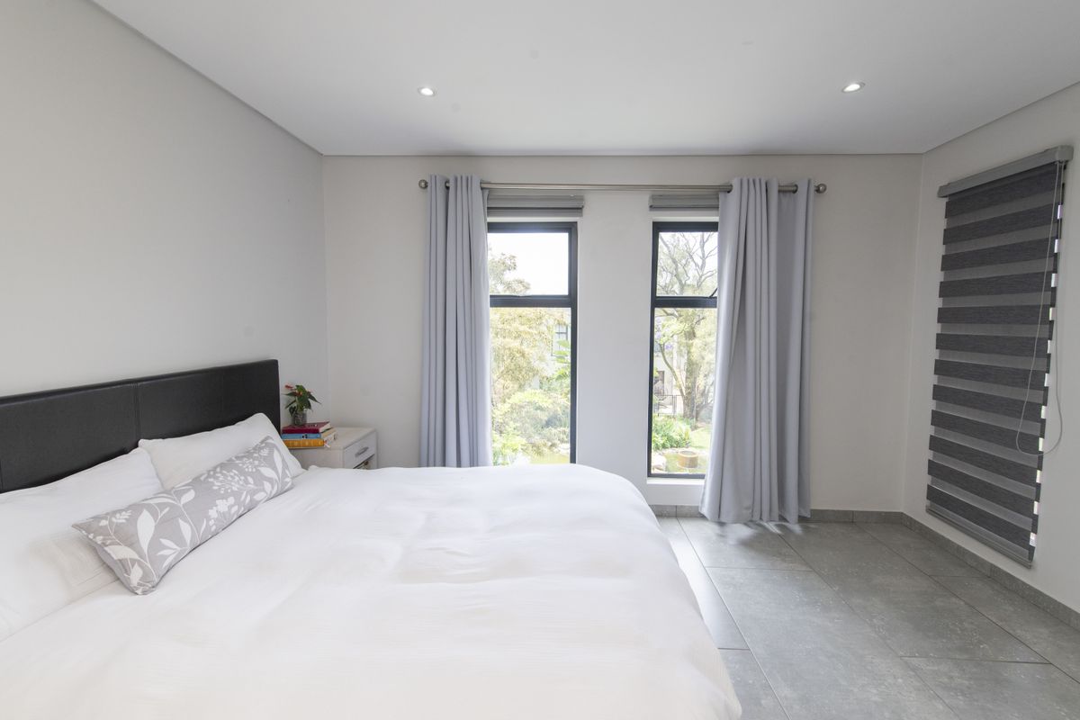 A bright and modern bedroom featuring large windows with sleek frames, tiled flooring, and recessed ceiling lighting.
