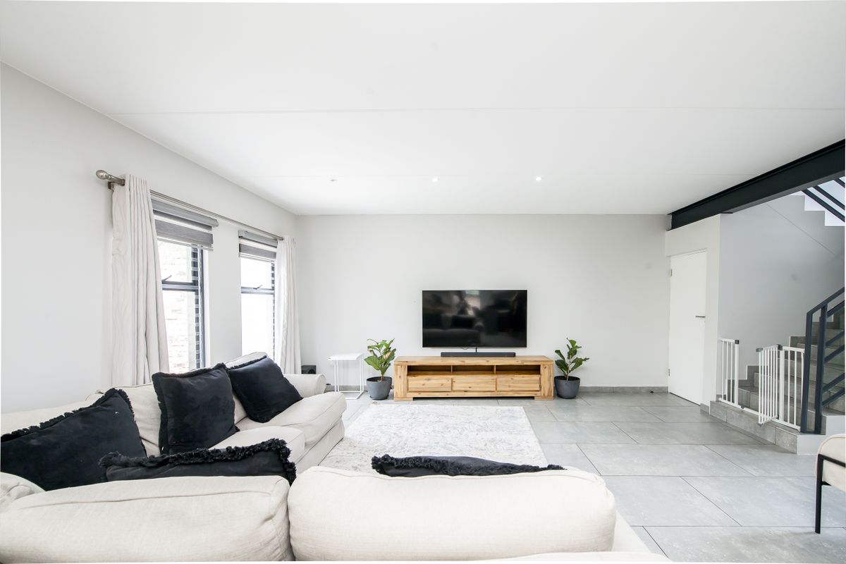A bright and spacious living room featuring large format floor tiles, recessed ceiling lighting, and an open-plan staircase with a modern metal balustrade.