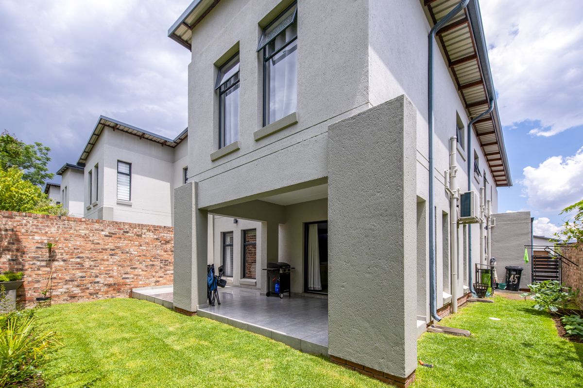 A view of the rear exterior of the townhouse, featuring a covered patio area, tiled flooring, and a private garden with a brick boundary wall.