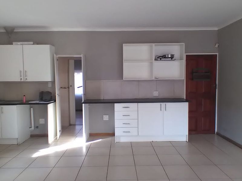 A functional kitchen area featuring white cabinetry, dark countertops, tiled splashbacks, and neutral floor tiles, offering a clean canvas for potential updates.