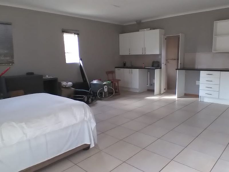 An open-plan living and kitchen area featuring tiled flooring, white built-in cabinetry, and laminate countertops, offering a functional space for living and dining.