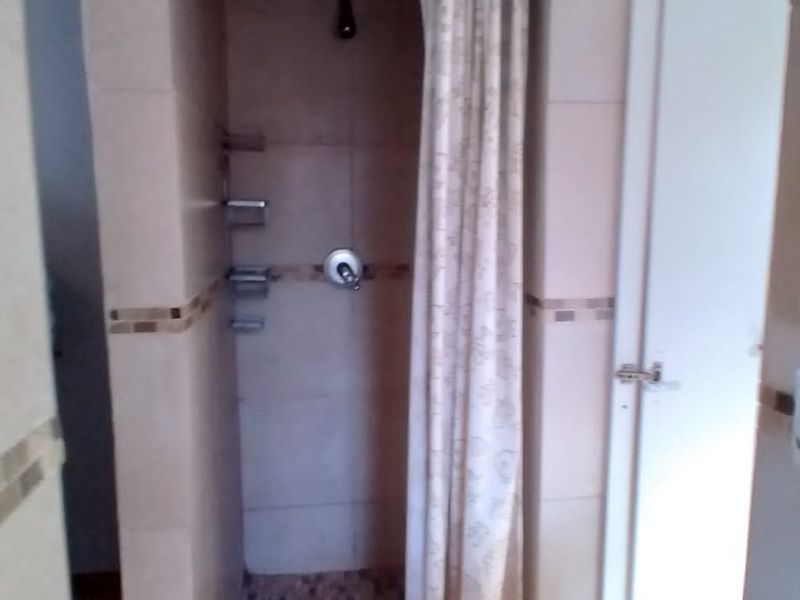 A functional bathroom featuring a tiled shower enclosure with a shower mixer and a vanity area with a mirror.