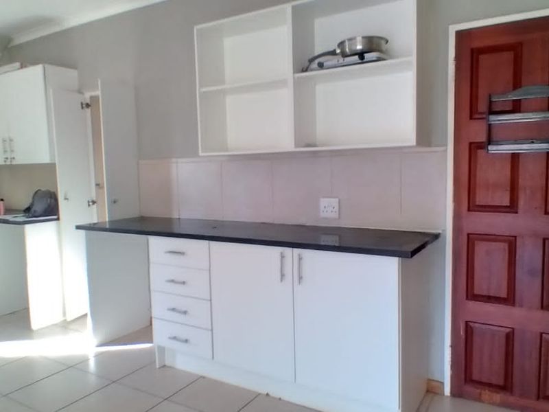 A functional kitchen area featuring white built-in cabinetry, dark laminate countertops, tiled backsplash, and tiled flooring, with a solid wood door entrance.