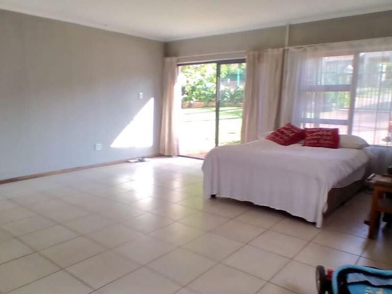 Spacious bedroom featuring neutral tiled flooring, large windows, and sliding glass doors providing direct access to the outdoor area.