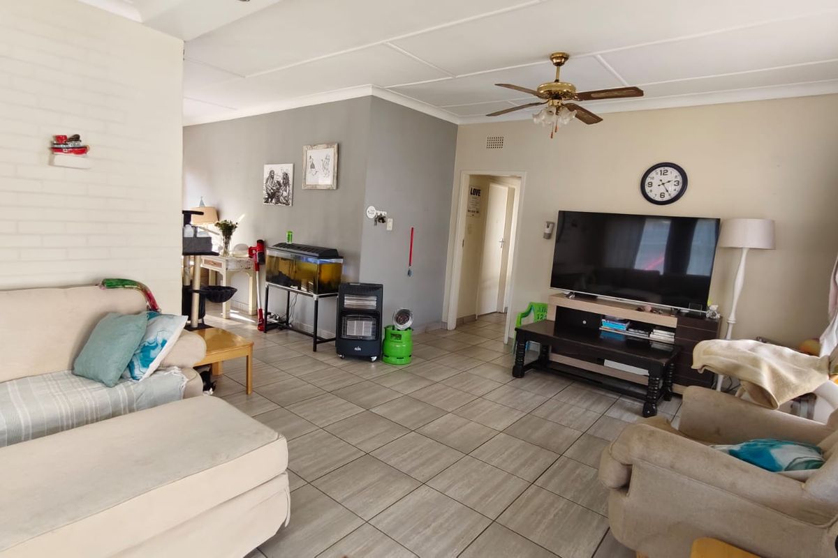 Spacious living room featuring neutral tiled flooring, a ceiling fan, and a painted brick accent wall, providing a comfortable and functional family living space.