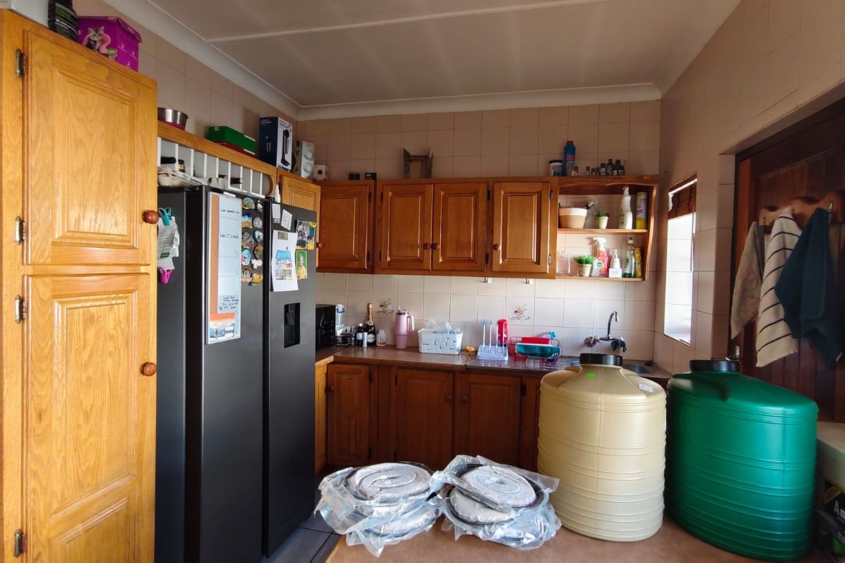 A functional kitchen featuring traditional wooden cabinetry, tiled splashbacks, and ample storage space, currently used for utility storage.