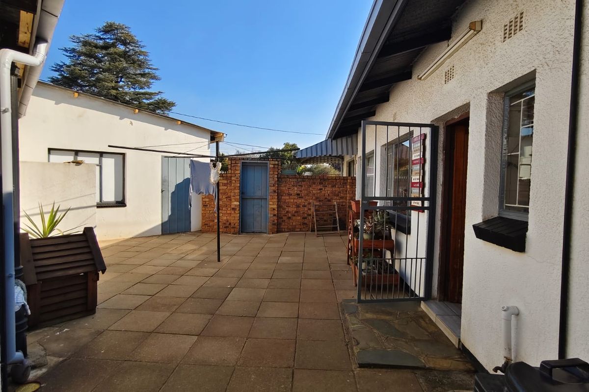 A paved rear courtyard area featuring a security gate, brick boundary wall, and access to the main dwelling and outbuilding.