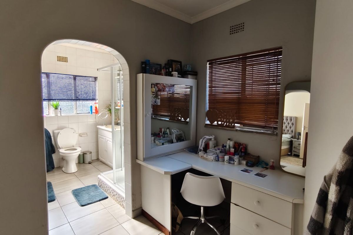 A bedroom featuring a built-in vanity desk and an arched doorway leading to an en-suite bathroom with a shower and toilet.