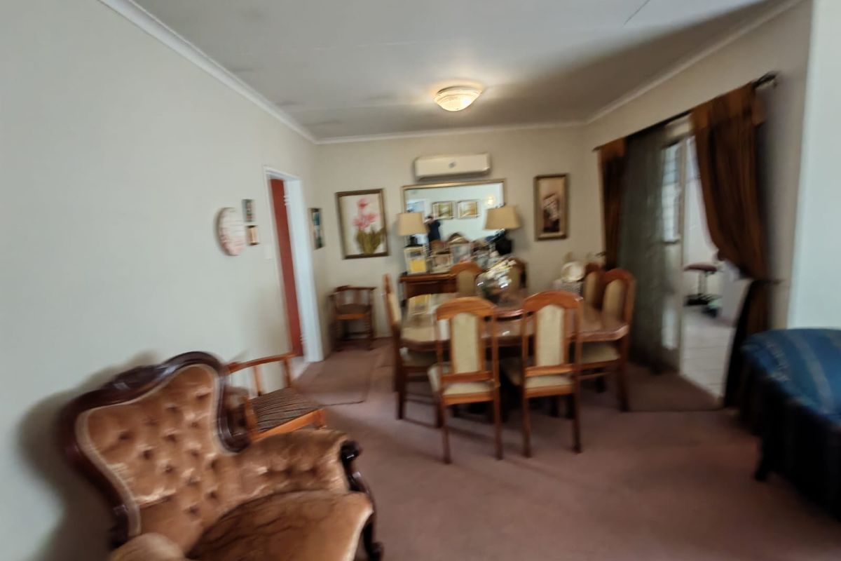 A dated dining and living area featuring wall-mounted air conditioning, carpeted flooring, and access to an adjacent space through sliding glass doors.