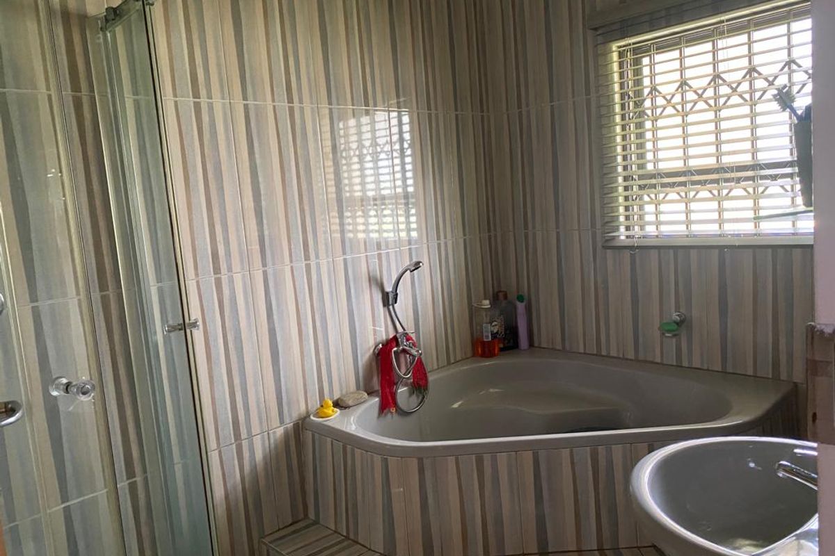 A functional bathroom featuring a corner bathtub, separate shower enclosure, and pedestal basin with full-height wall tiling.