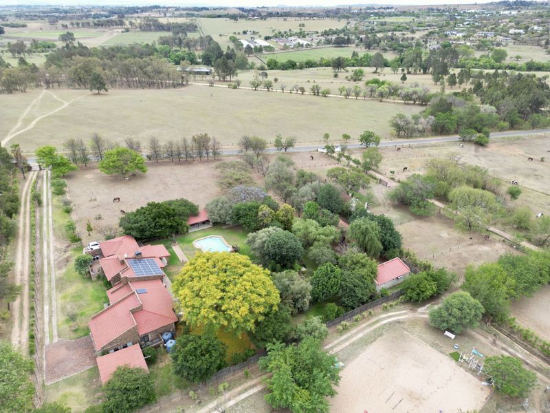 Aerial view of a rural property featuring a main residence with solar panels, a swimming pool, and extensive landscaped grounds.