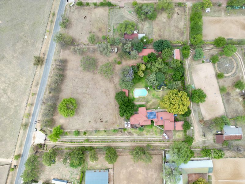 Aerial view of a large rural property featuring a main residence with solar panels, a swimming pool, and extensive landscaped grounds.