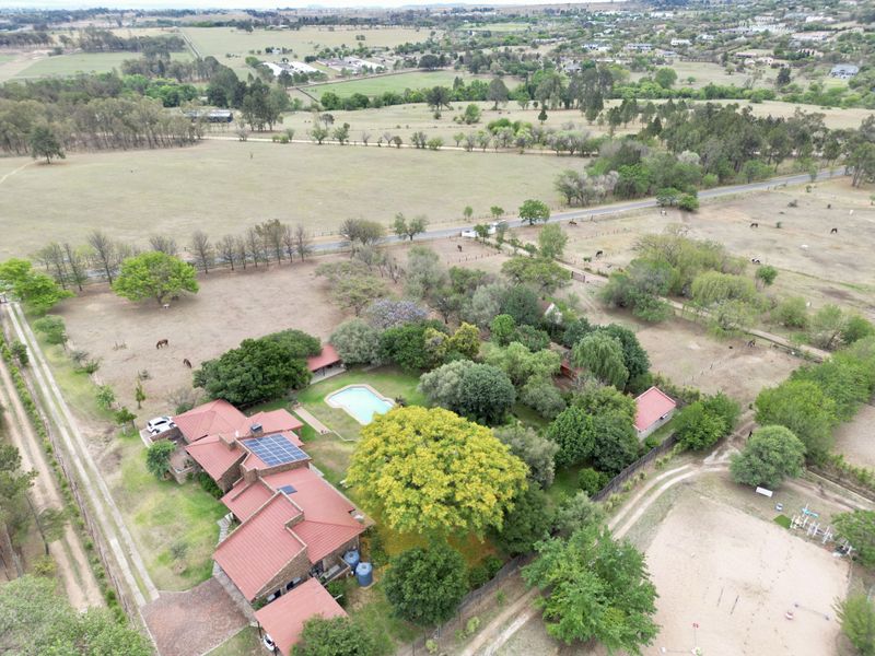 Aerial view of a residential property featuring a swimming pool, solar panels, and extensive landscaped grounds in a rural setting.