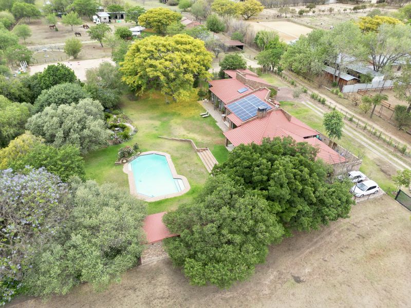Aerial view of a residential property featuring a swimming pool, expansive garden, and a house equipped with solar panels and a metal roof.