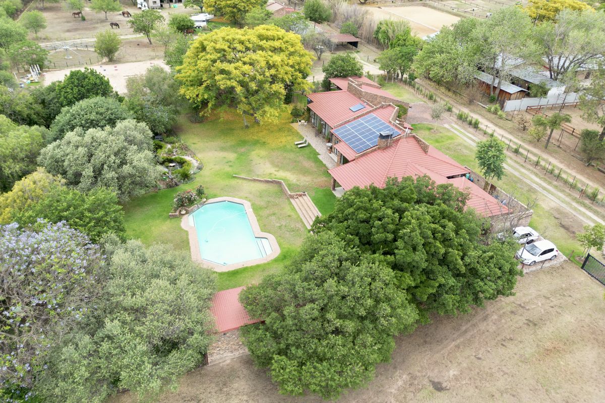 Aerial view of a residential property featuring a swimming pool, expansive garden, and a house equipped with solar panels and a metal roof.