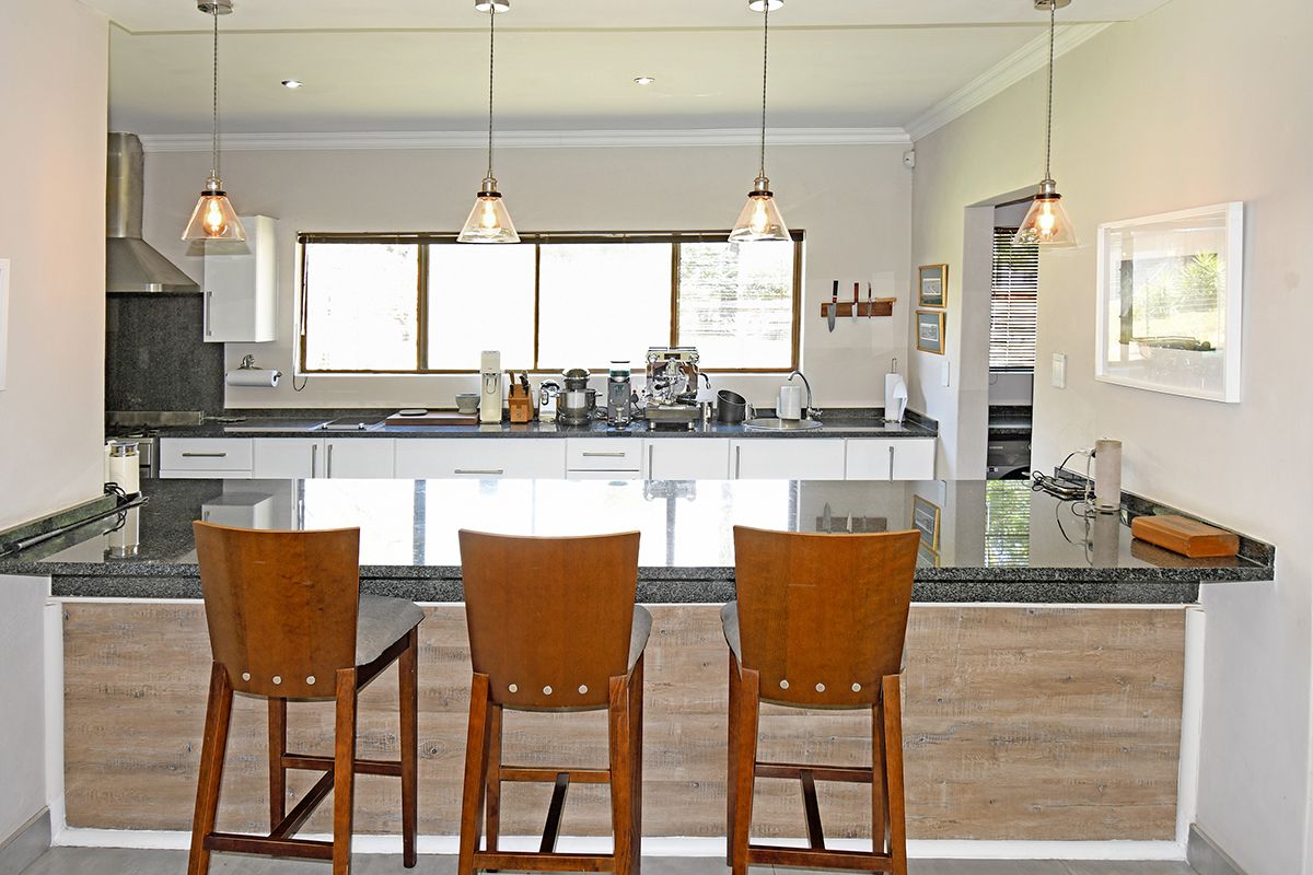 Modern kitchen featuring a spacious granite breakfast bar, sleek white cabinetry, stainless steel extractor fan, and elegant pendant lighting.