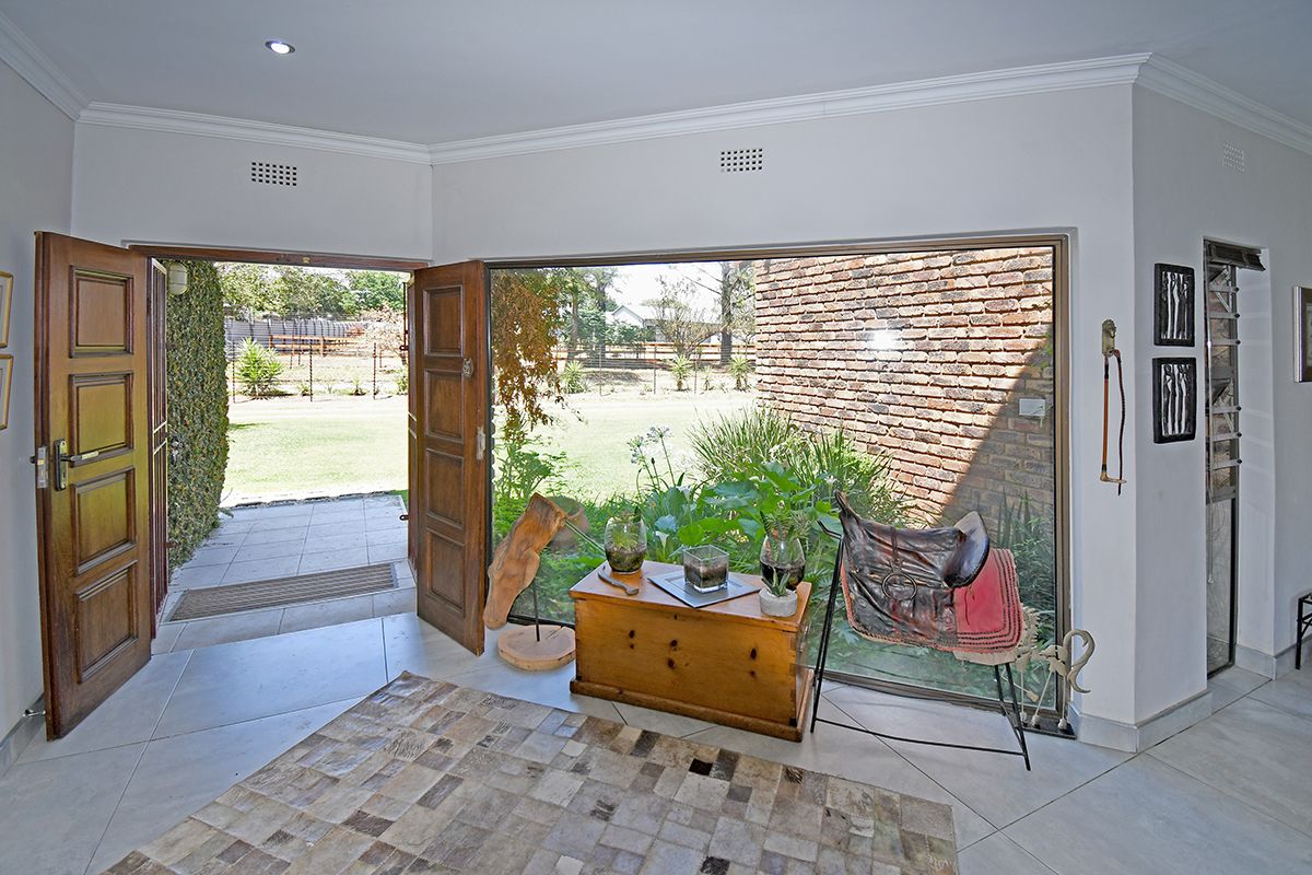 A bright living area featuring large glass sliding doors that open onto a garden patio, with neutral tiled flooring and recessed lighting.