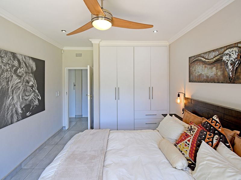 A well-maintained bedroom featuring built-in cupboards, tiled flooring, and a modern ceiling fan, offering a clean and functional living space.