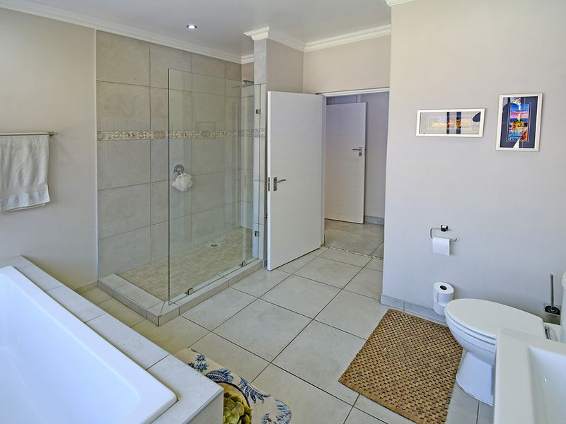 A well-maintained bathroom featuring a walk-in glass shower, built-in bathtub, and neutral floor-to-ceiling tiling with modern fixtures.