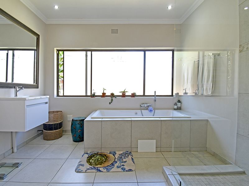 A modern, well-maintained bathroom featuring a built-in bathtub, wall-mounted vanity, and a glass-enclosed shower area with neutral tiling throughout.