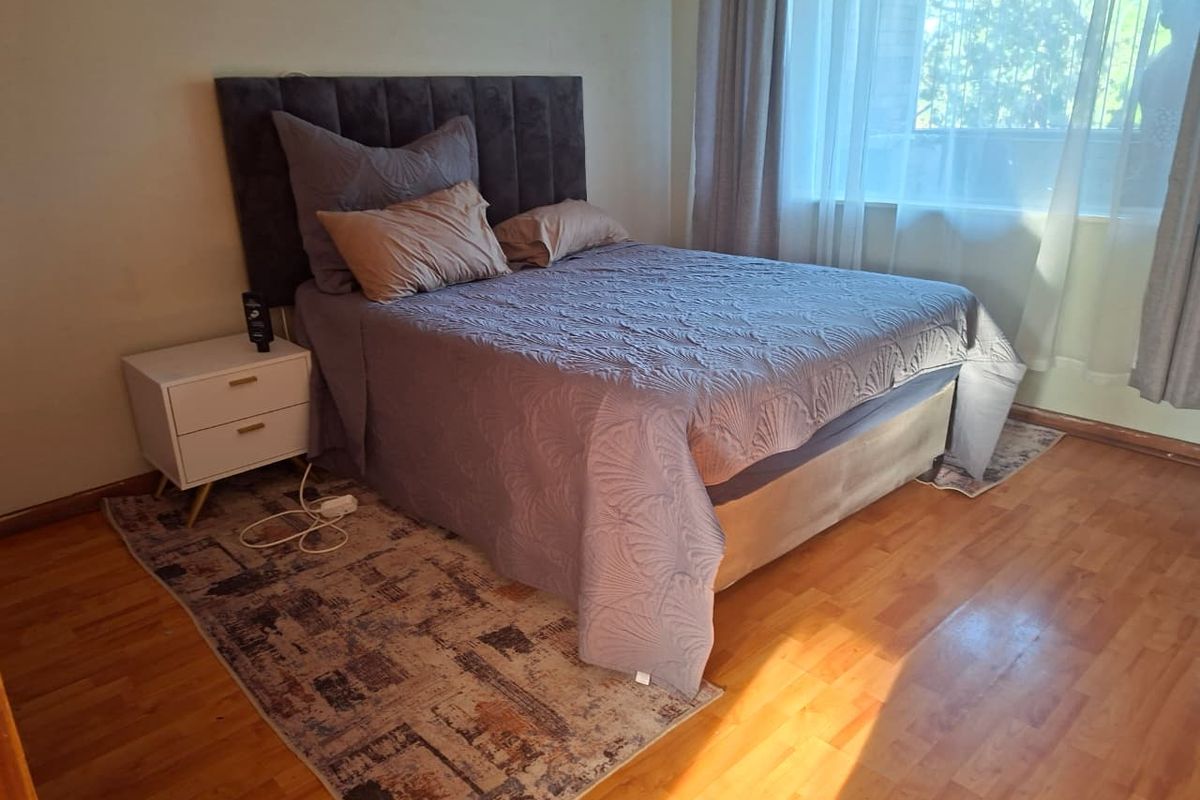 A bedroom featuring laminate wood flooring and a large window with curtains, providing natural light.