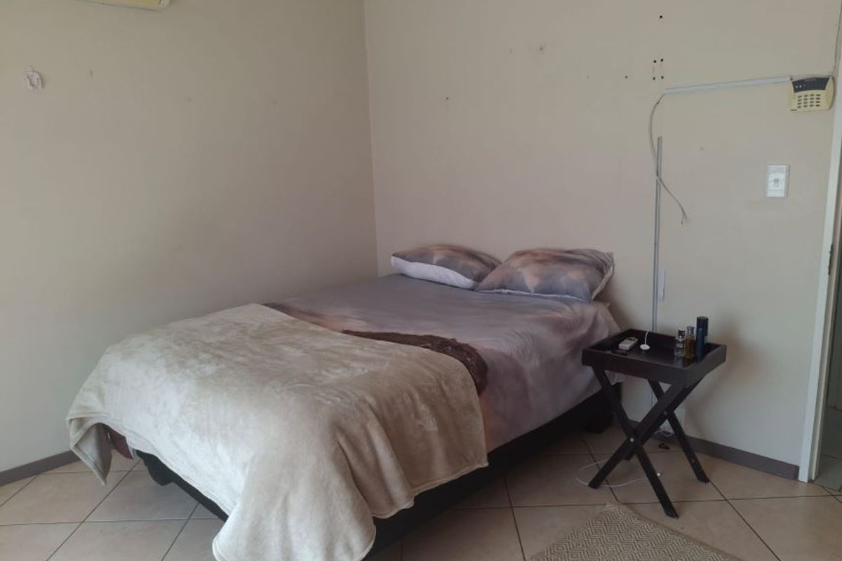 A bedroom featuring tiled flooring and a wall-mounted air conditioning unit, currently showing signs of wear on the walls and exposed alarm wiring.