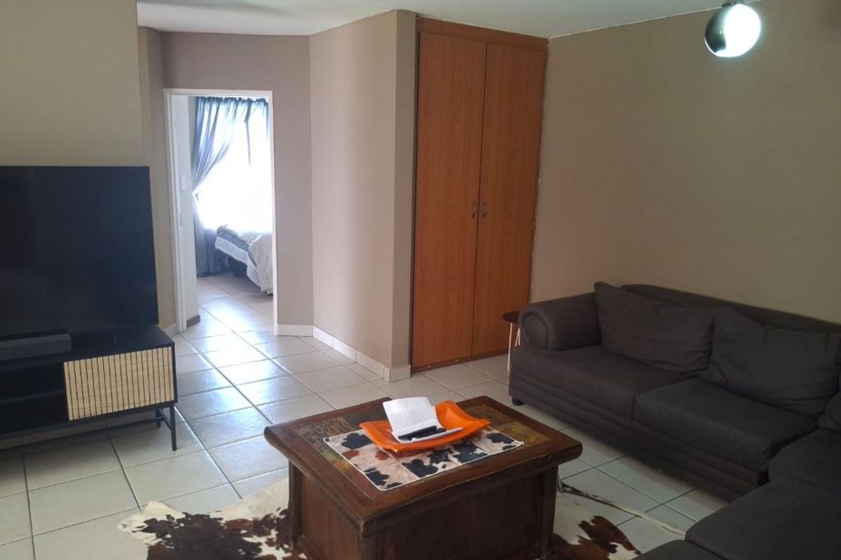 A living room featuring tiled flooring, a built-in cupboard, and a pendant light, with an adjacent view into a bedroom.