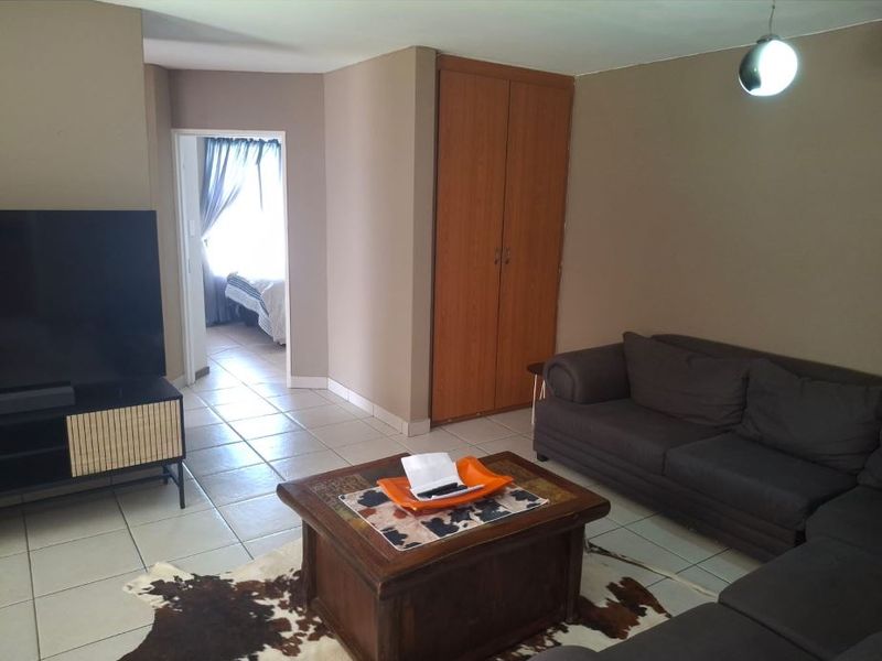 A living room featuring tiled flooring, a built-in cupboard, and a pendant light, with an adjacent view into a bedroom.