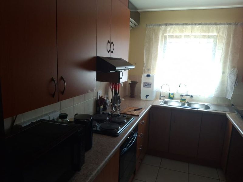 A functional kitchen featuring laminate cabinetry, built-in electric hob and oven, extractor fan, and a double bowl stainless steel sink with tiled finishes.