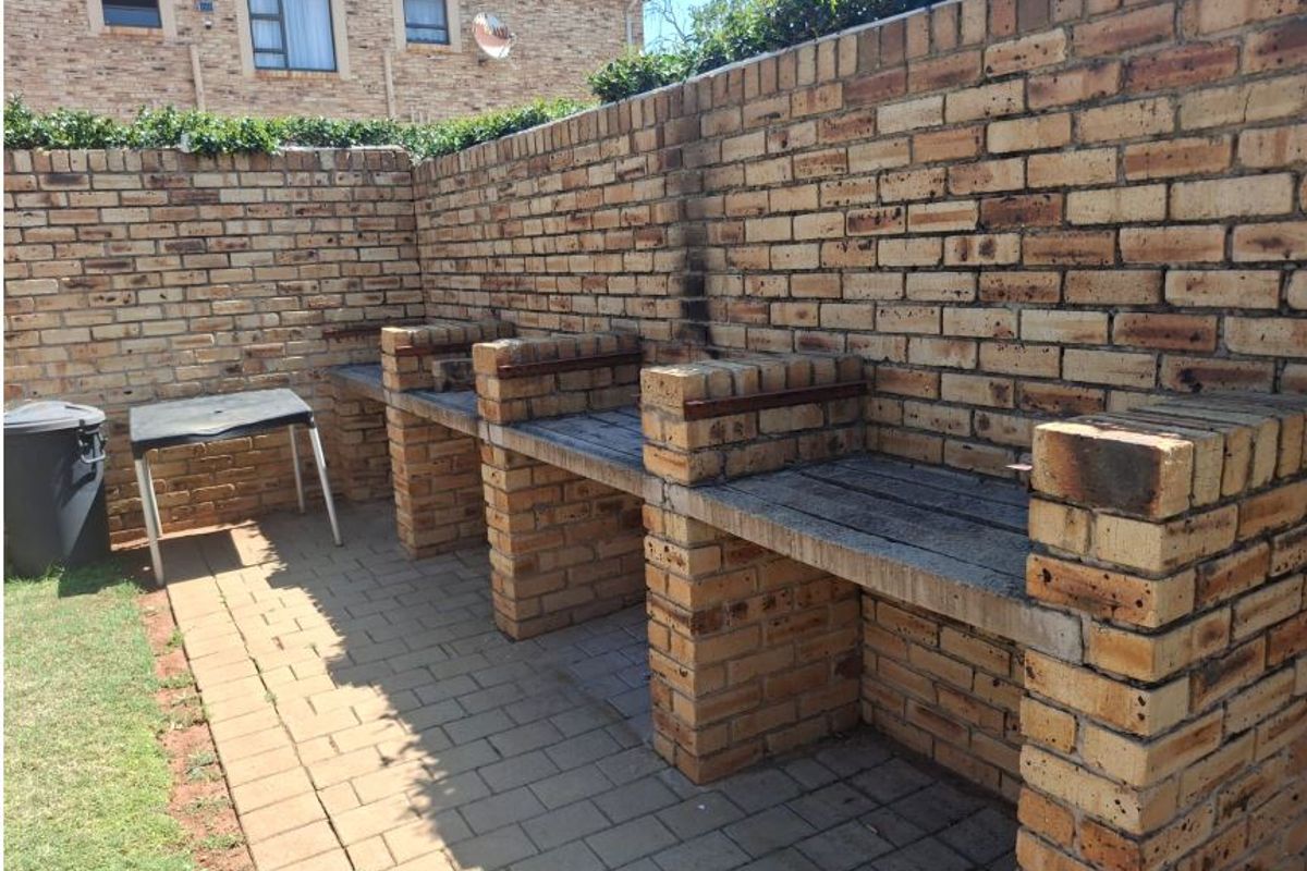Outdoor entertainment area featuring a substantial built-in brick braai station, paved flooring, and enclosed by a high brick perimeter wall.