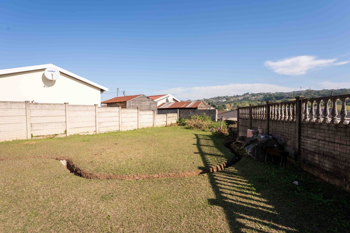 A rear garden area featuring a lawn, precast concrete boundary walls, and a decorative balustrade wall section.