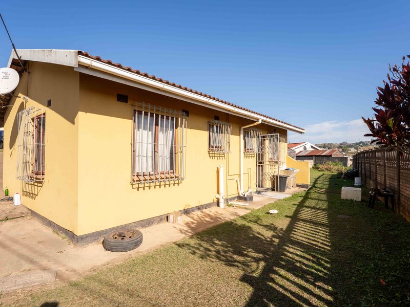 Rear view of the house featuring a tiled roof, security bars on windows, and a concrete apron with an external wash basin.